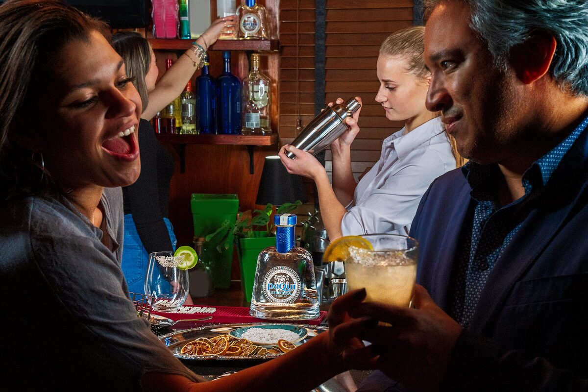 Bar scene with PaQui Tequila, bartender shaking cocktails for guests